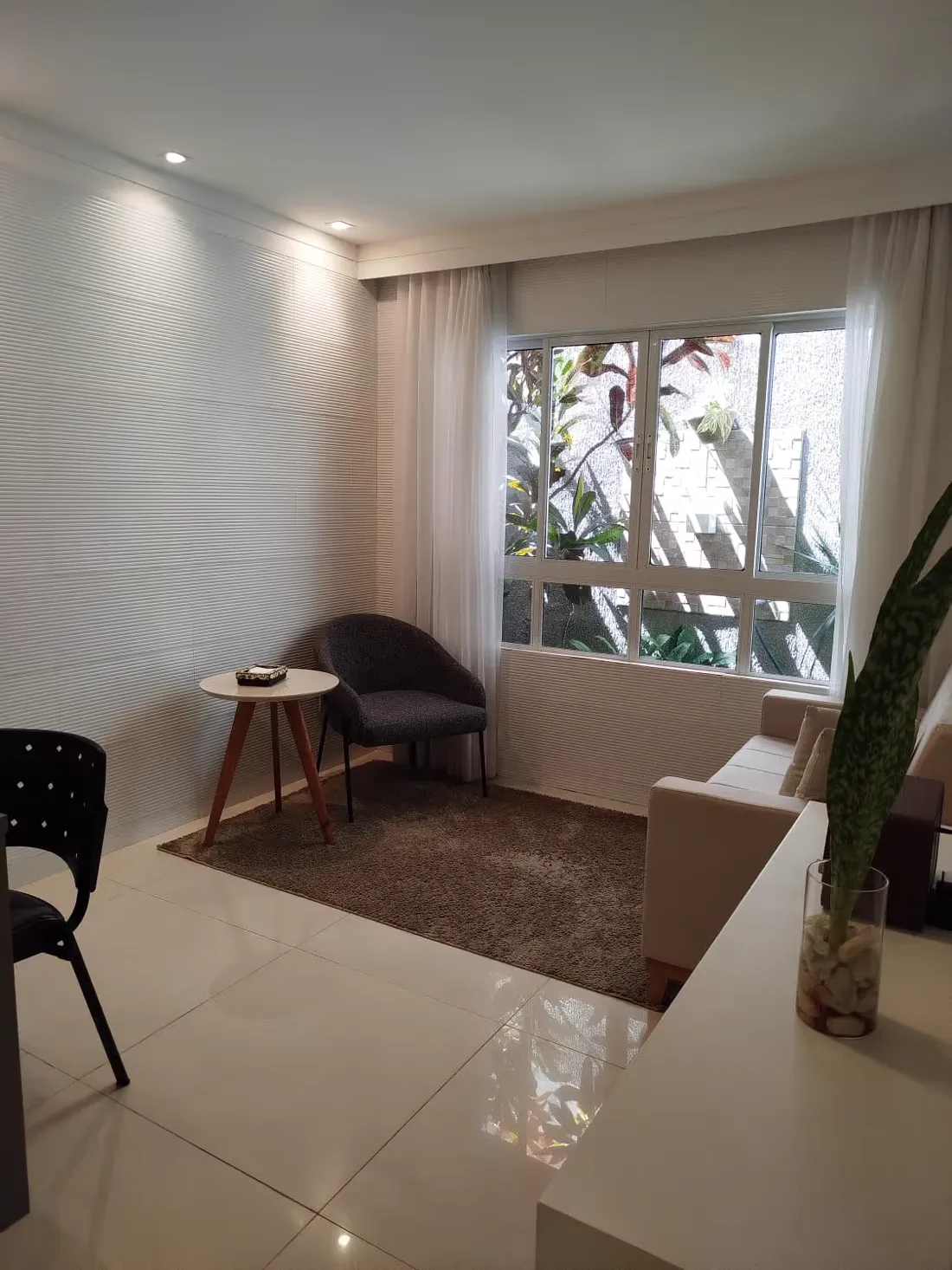 Sala iluminada por janela, com poltronas e plantas